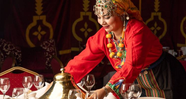 Mujer con vestimenta tradicional preparando una mesa en un interior decorado.