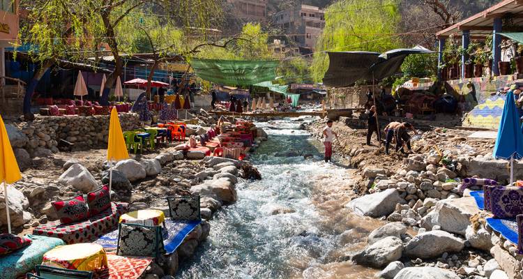 Des cafés colorés au bord de la rivière et des étals de marché bordent un torrent de montagne où les habitants et les touristes se détendent sur des coussins colorés.