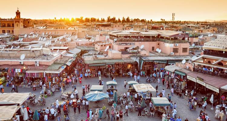 A bustling market square during sunset, with many people and market stalls.