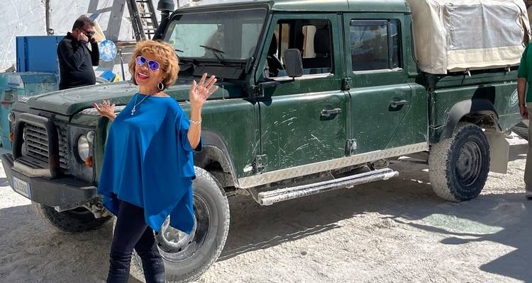 Voyageur souriant posant à côté d'un robuste 4x4 dans une carrière de marbre éclatante avec de la poussière blanche sous les pieds.