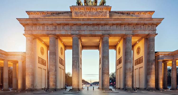 La porte de Brandebourg illuminée brille au crépuscule avec un ciel clair derrière elle.