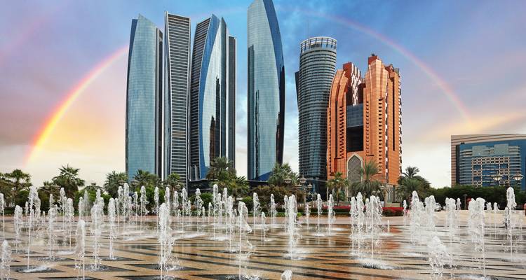 Gratte-ciel modernes à Abu Dhabi avec un arc-en-ciel et une fontaine d'eau au premier plan.