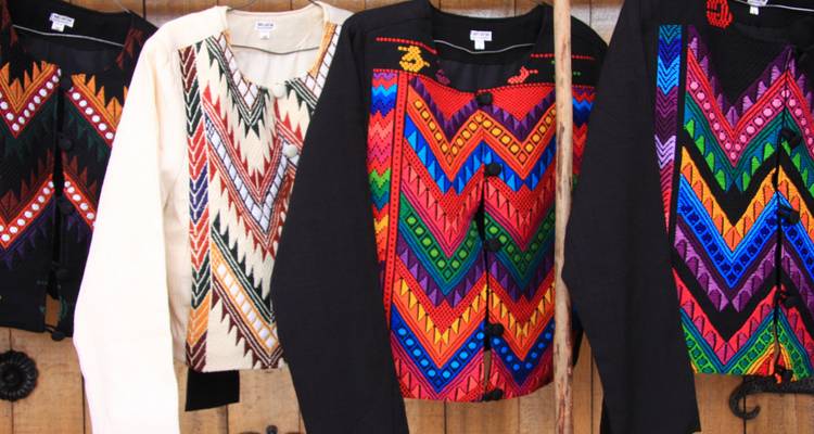 Kleurrijke geweven kledingstukken die hangen ter uitstalling.