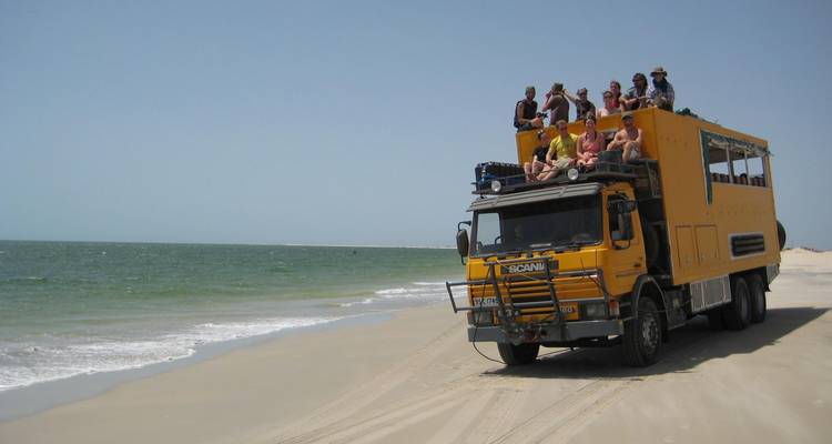 Groupe de personnes assises sur le toit d'un camion tout-terrain sur une plage de sable.