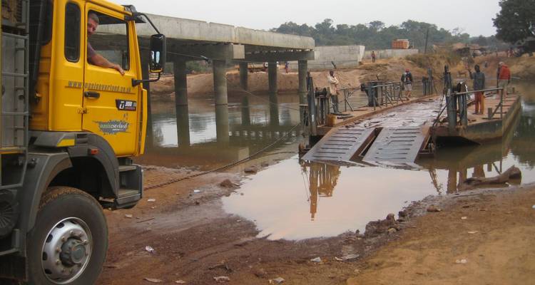 Camion tout-terrain près d'un pont de fortune au-dessus d'une rivière.