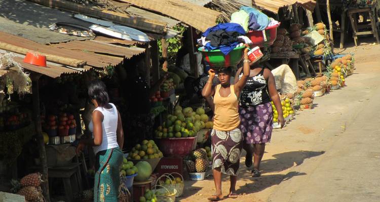 Scène de marché local avec deux femmes portant des marchandises sur leur tête.