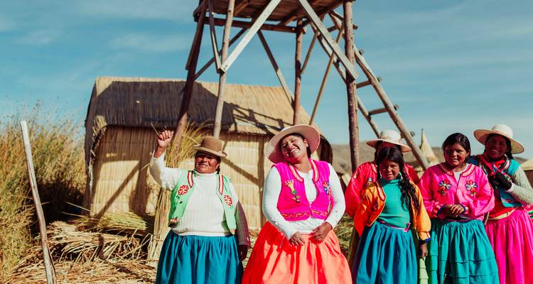 Mujeres indígenas sonrientes con coloridas faldas tradicionales posan en la isla flotante de juncos Uros.