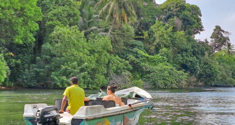 Deux personnes sur un bateau dans une rivière entourée d'une végétation luxuriante.