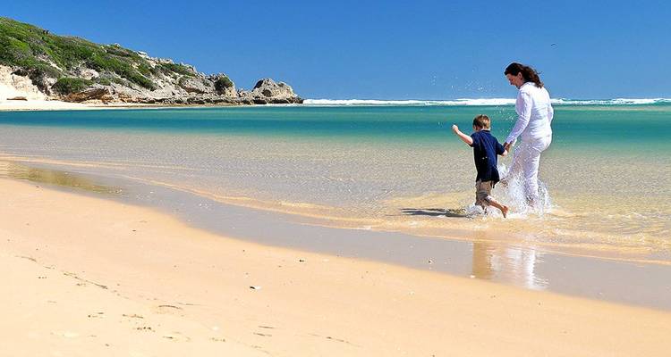 Mutter und Kind planschen in dem seichten türkisfarbenen Wasser eines ruhigen Sandstrandes.