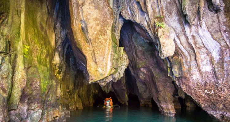 Des gens dans des bateaux près de l'entrée d'une grande grotte.