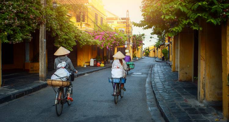Fietsers op de straat van een traditionele stad met gele gebouwen.