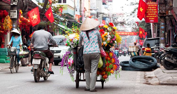 Straatbeeld met een persoon die een kar vol bloemen duwt in Hanoi.