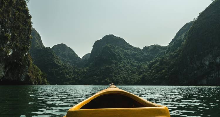 Kajak navigiert durch grünes Wasser, umgeben von hoch aufragenden Kalkstein-Karst-Formationen.