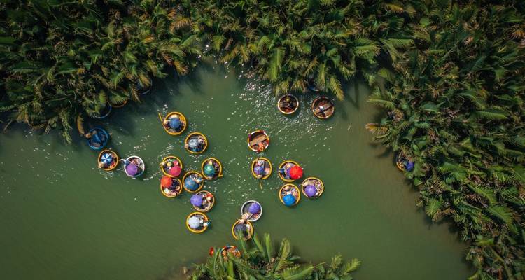Vue aérienne de bateaux-paniers traditionnels flottant sur une rivière aux eaux vertes luxuriantes.