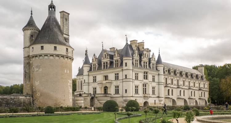 Un château pittoresque avec des jardins paysagers sous un ciel nuageux.