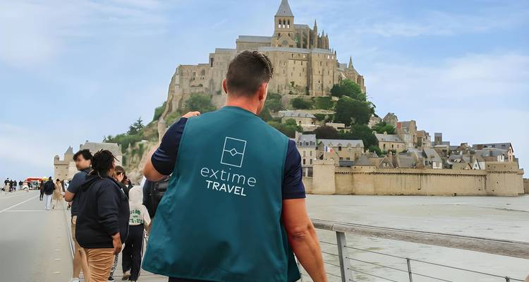 Los participantes del tour caminan hacia Mont Saint-Michel liderados por una guía con chaleco azul turquesa en un día despejado