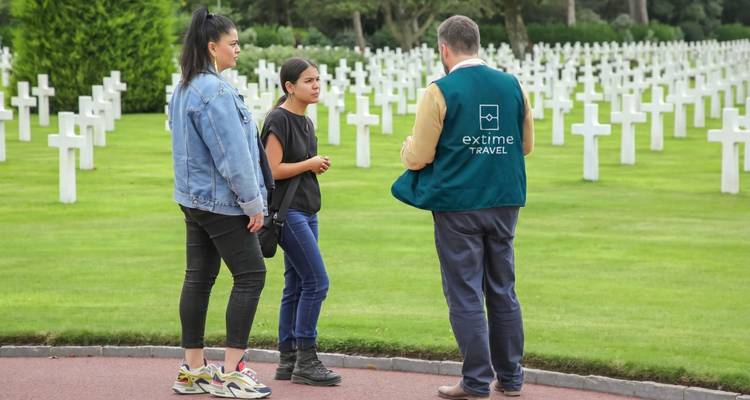 Un pequeño grupo se encuentra entre filas de cruces blancas en el Cementerio Americano de Normandía