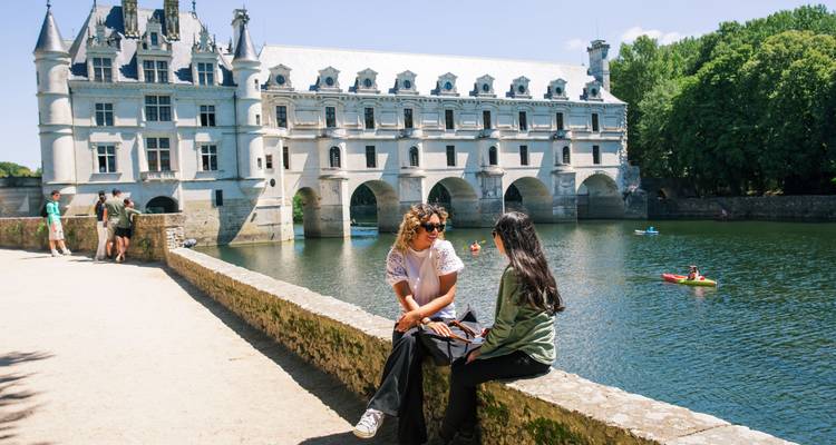 Los viajeros se relajan junto al río Cher con los arcos del Château de Chenonceau reflejándose en el agua