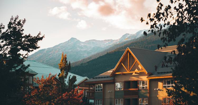 Huizen en bomen met bergen op de achtergrond tijdens zonsondergang.