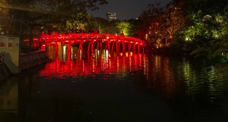 Brücke mit roten Lichtern beleuchtet in der Nacht, die sich im Wasser spiegeln und eine lebendige Atmosphäre schaffen.