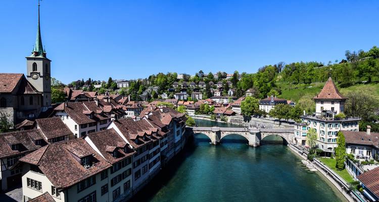 Paysage urbain avec rivière et ponts entourés de verdure.
