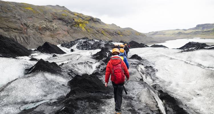 Personas caminando en un glaciar rodeado de rocas volcánicas negras y hielo.