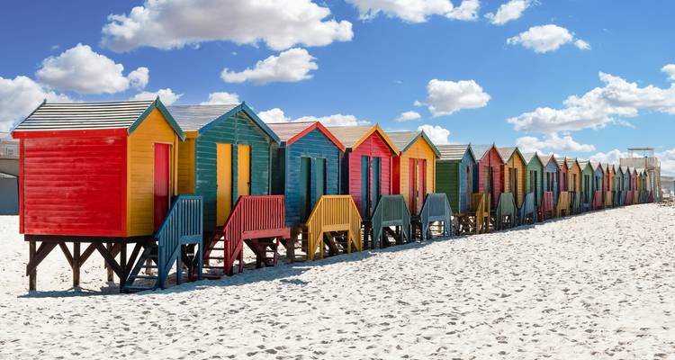 Cabanes de plage colorées alignées sur une plage de sable.