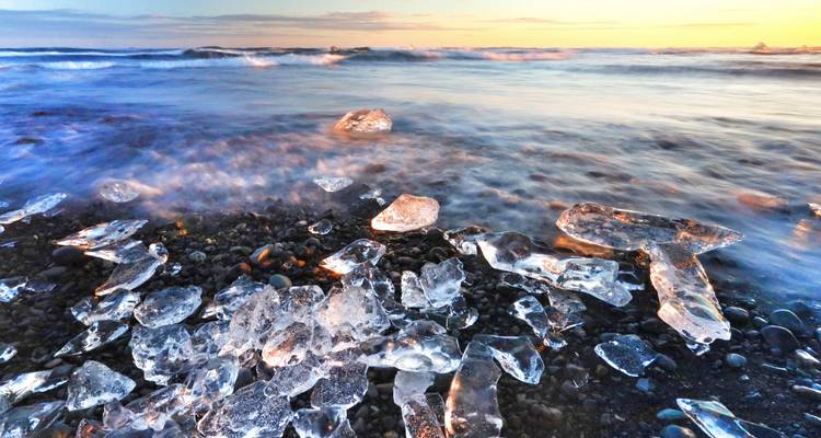 Gletschereis am schwarzen Sandstrand während des Sonnenuntergangs.