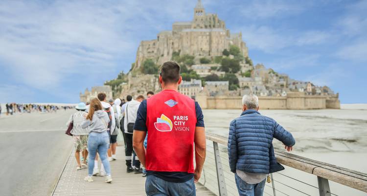 Groupe touristique près du Mont Saint-Michel avec guide portant un gilet rouge
