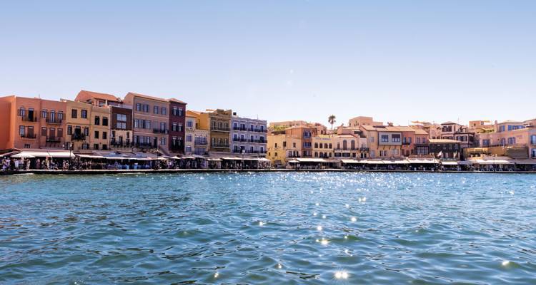 Farbenfrohe venezianische Hafengebäude säumen die glitzernden blauen Gewässer von Chania an einem sonnigen Tag.