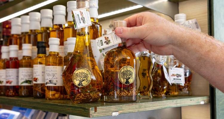 Eine Hand waehlt eine Flasche lokal hergestelltes infundiertes Olivenoel aus einer Ausstellung handwerklicher Produkte aus.