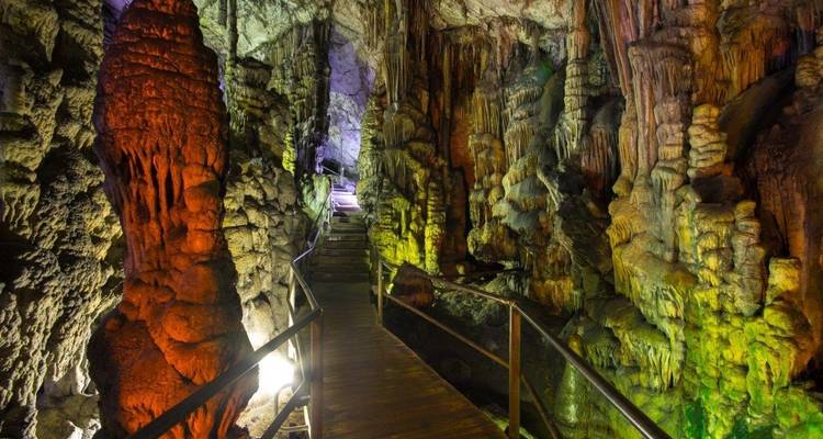 Verlichte grotingang met kleurrijke stalactieten en stalagmieten.