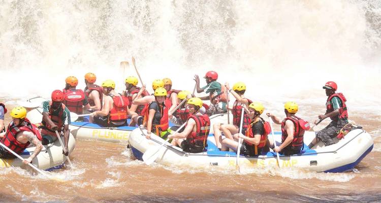 Gruppe von Menschen beim Rafting auf einem Fluss mit einem Wasserfall im Hintergrund.