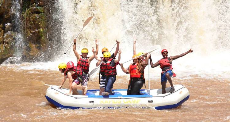 Aufgeregte Gruppe von Menschen, die auf einem Floß in Wildwasser-Stromschnellen posiert.