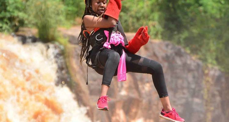 Frau in der Luft, die ein Zipline-Abenteuer genießt, mit Grün im Hintergrund.