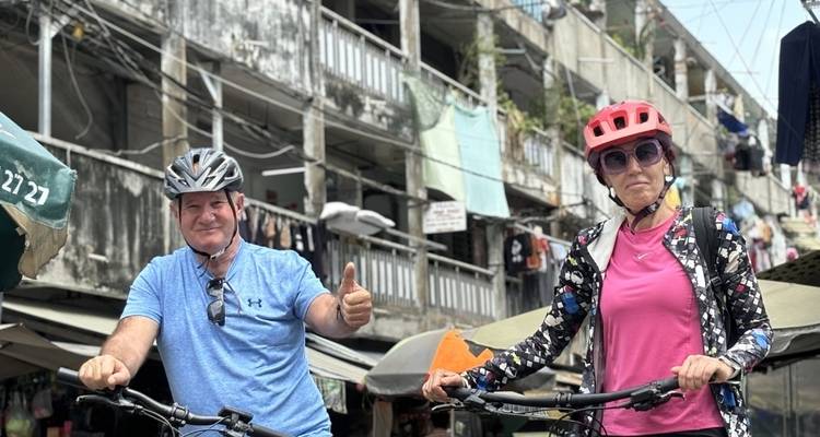 Zwei lächelnde Menschen auf Fahrrädern vor städtischer Architektur.