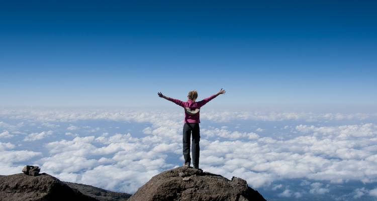 Personne debout sur un rocher avec les bras étendus au-dessus des nuages.
