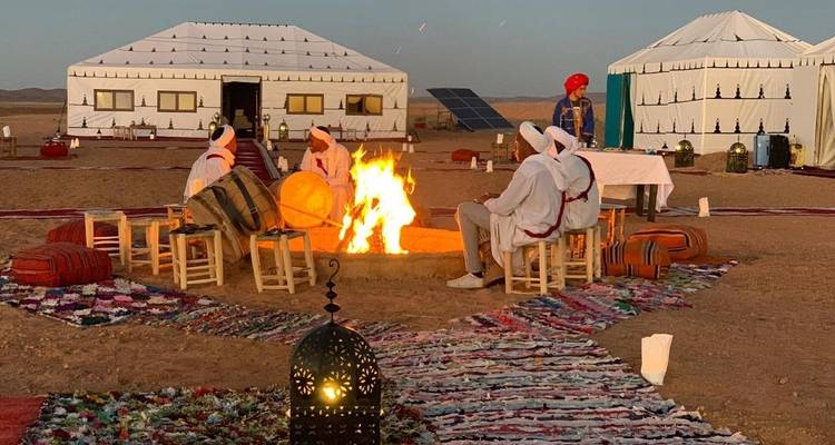 Traditionelle Berber-Musiker in weißen Gewändern sitzen um ein loderndes Lagerfeuer in einem Zeltlager der Sahara-Wüste.