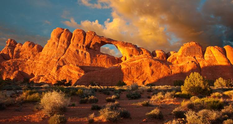 Rode rotsformaties onder een lucht met zonsondergangwolken.