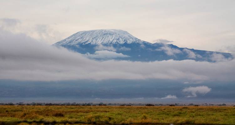 Le mont Kilimandjaro enneigé avec des nuages et des champs à proximité.