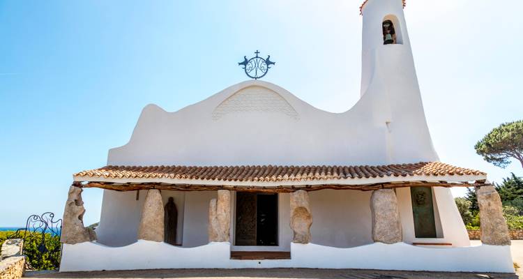 Église Stella Maris blanchie à la chaux à Porto Cervo avec des courbes organiques, un toit en tuiles et des vues sur la mer.