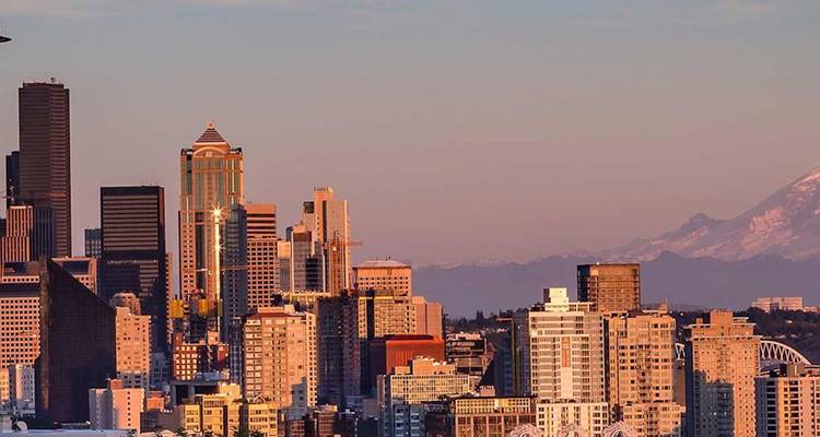 Seattles Skyline, die im warmen Sonnenlicht leuchtet, mit dem schwach sichtbaren Mount Rainier.