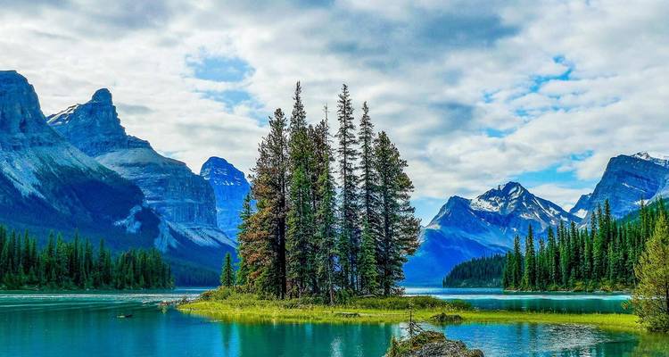 Lac turquoise avec une minuscule île de conifères entourée de pics escarpés aux sommets enneigés et de forêt.