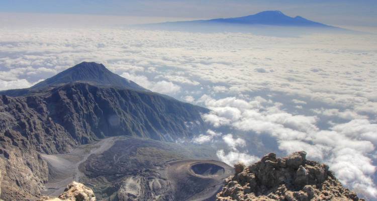 Aerial view showcasing volcanic craters and mountains rising through clouds.