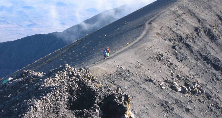 A hiker with a backpack walking on a mountain trail with rocky terrain.