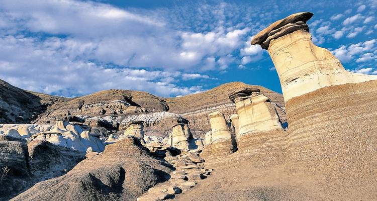 Geërodeerde hoodoos en gelaagde badlands rotsformaties rijzen op onder een gepatrooneerde blauwe hemel.