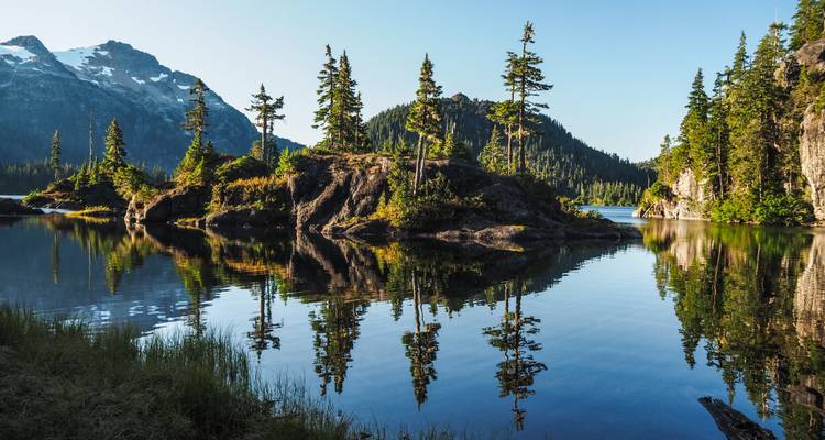 Lac serein entouré de montagnes boisées avec des reflets.