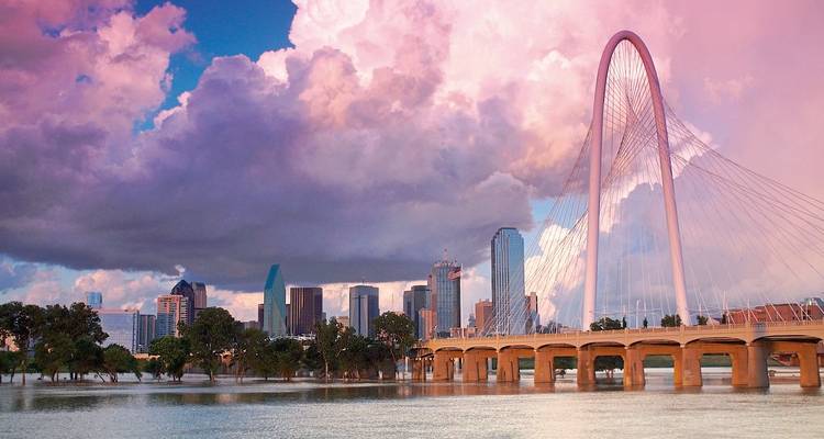 A scenic view of a bridge and Dallas skyline under dramatic clouds.
