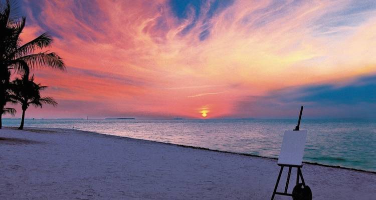 Beach scene at sunset with an easel on the sand.