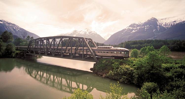 Train sur un pont au-dessus d'une rivière avec des montagnes.